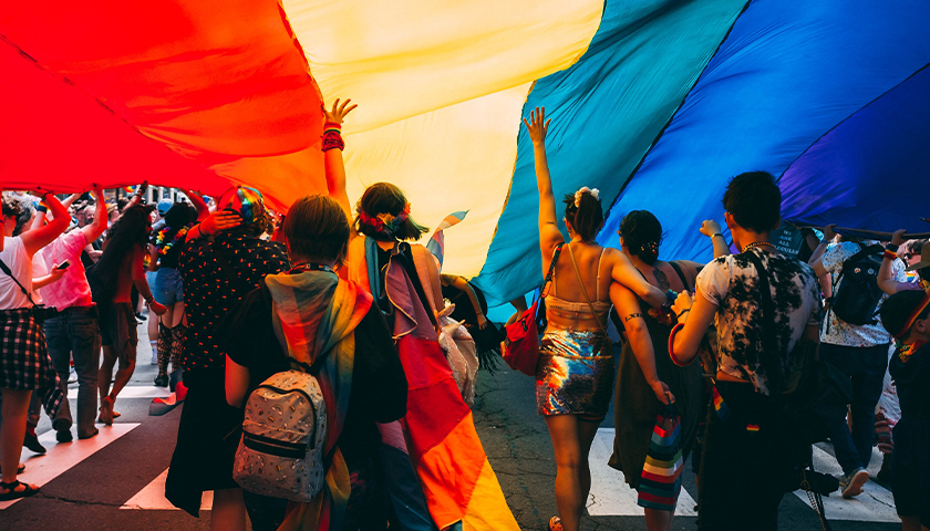 Pride Parade with group of people under large rainbow flag