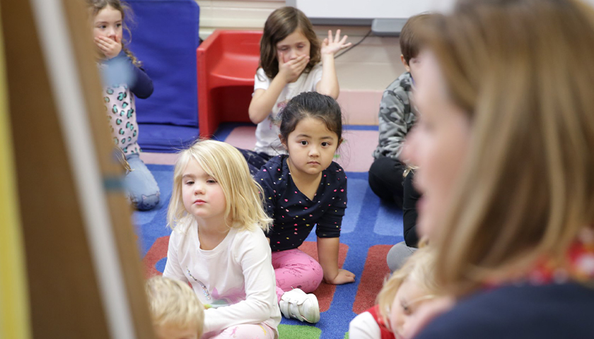 Students on the floor in the classroom, listening to the teacher read