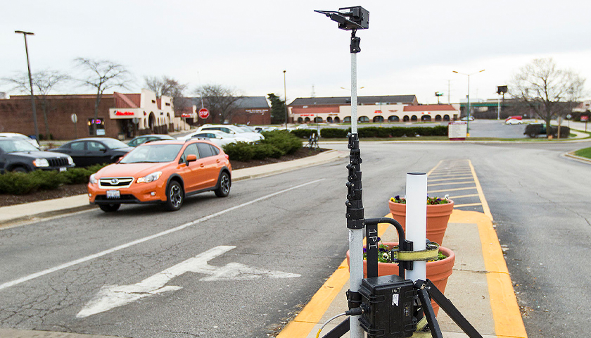 A portable tripod-mounted Miovision Automatic License Plate Recognition data acquisition camera is set up at an intersection in suburban Illinois.