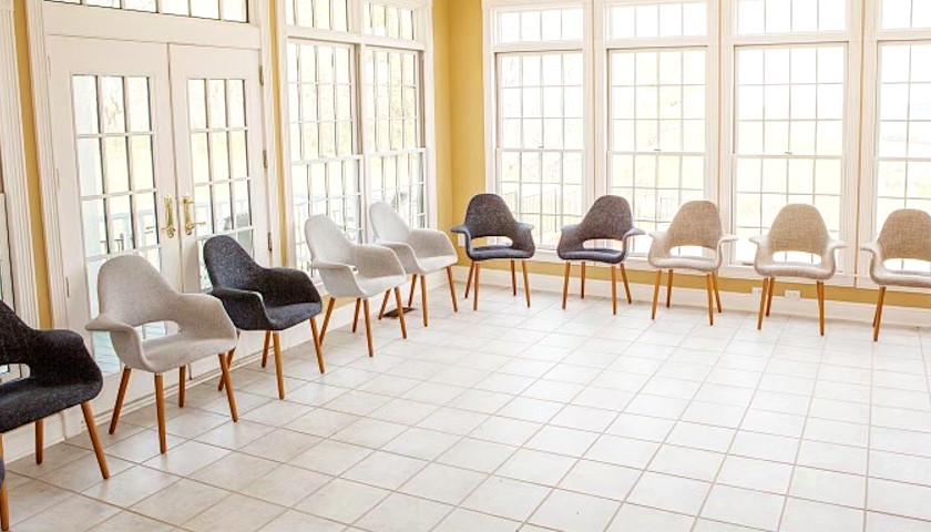 A bright room with large windows and a circle of modern chairs arranged along the walls